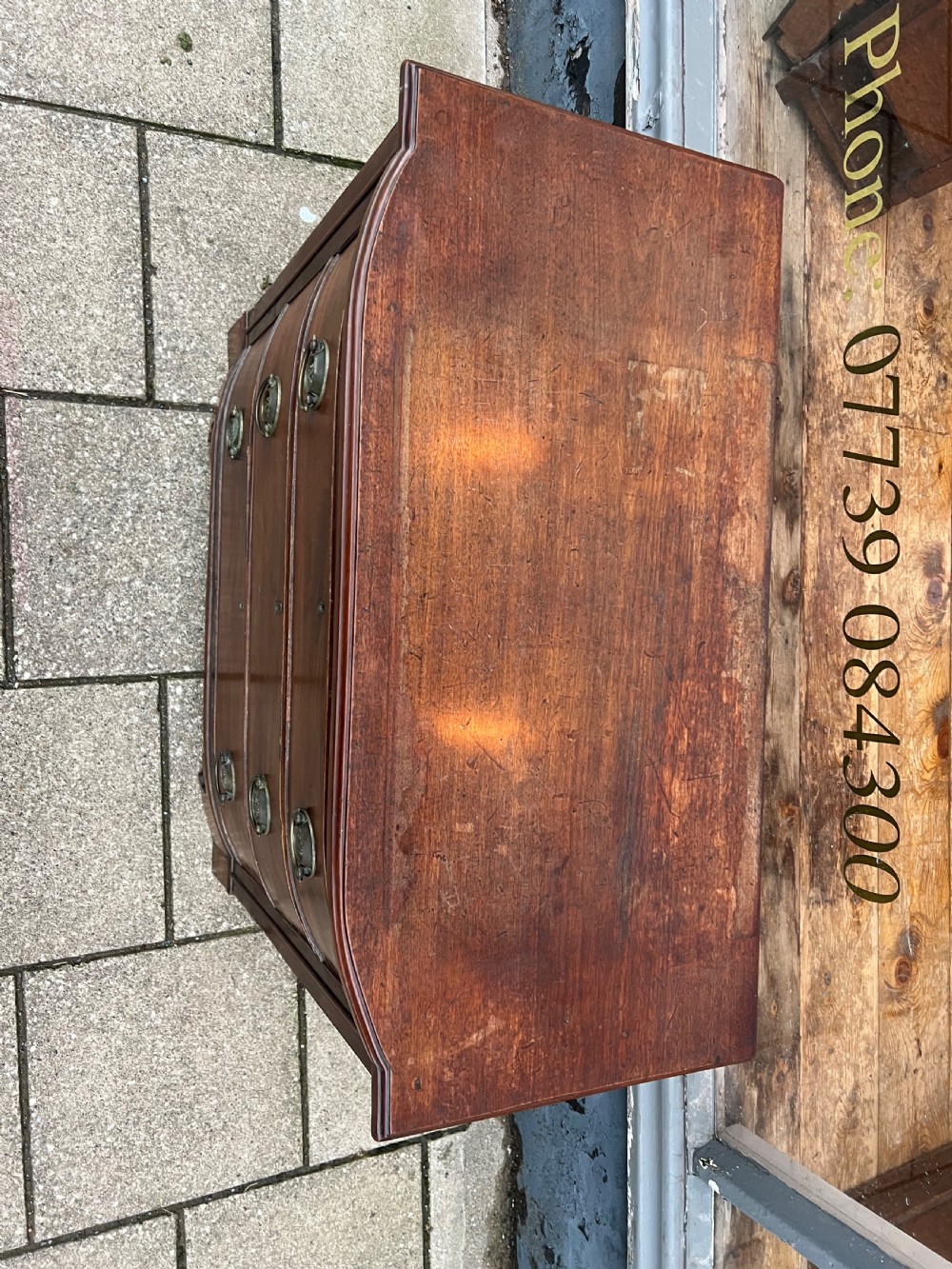 A small Georgian mahogany bow-front chest of three drawers featuring circular brass ring pulls and bracket feet. View IV
