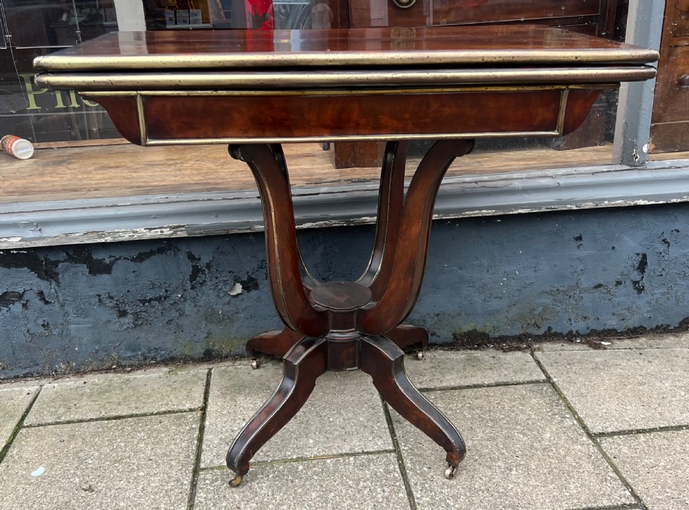 A Regency mahogany card table with brass edging, fold-over top, and quadform pedestal base on castors. View V
