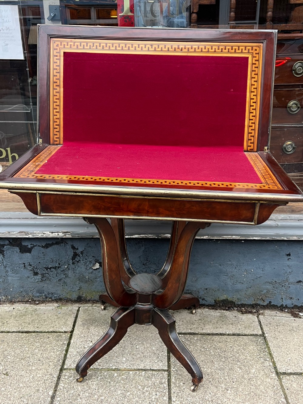A Regency mahogany card table with brass edging, fold-over top, and quadform pedestal base on castors. View IX