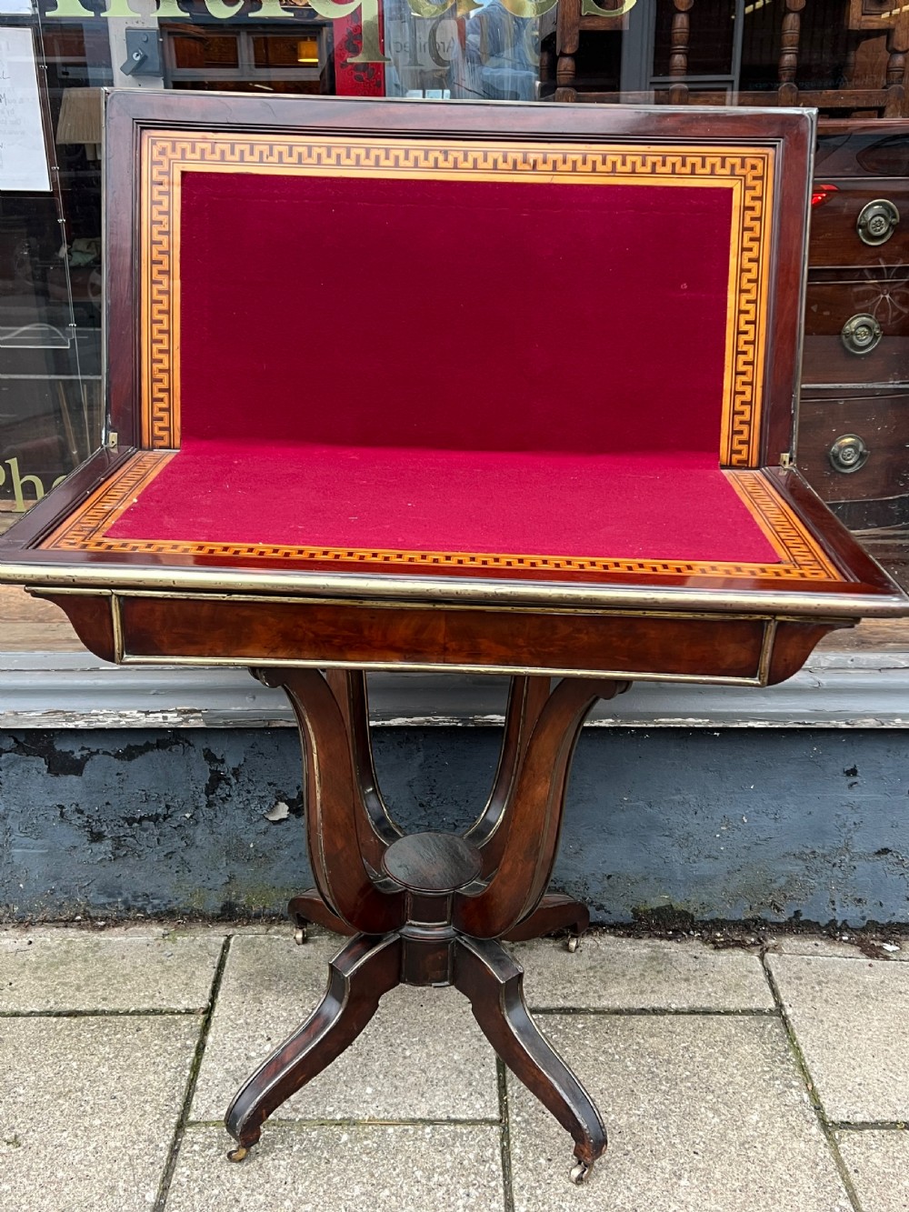 A Regency mahogany card table with brass edging, fold-over top, and quadform pedestal base on castors. View X