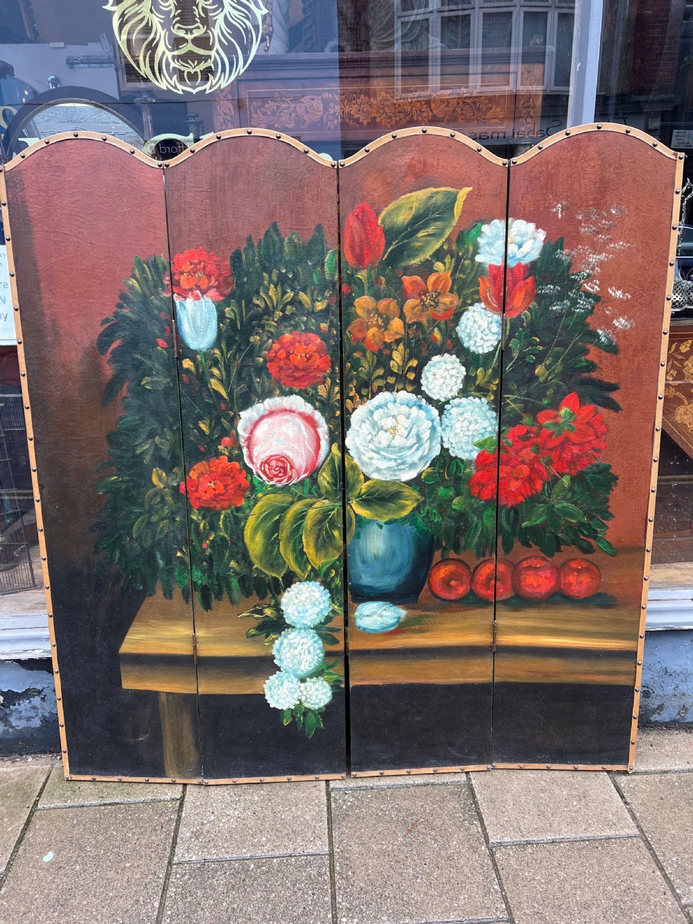 A four-panel arched folding screen featuring a large hand-painted floral still life in a blue vase set on a wooden table surface against a warm brown background.