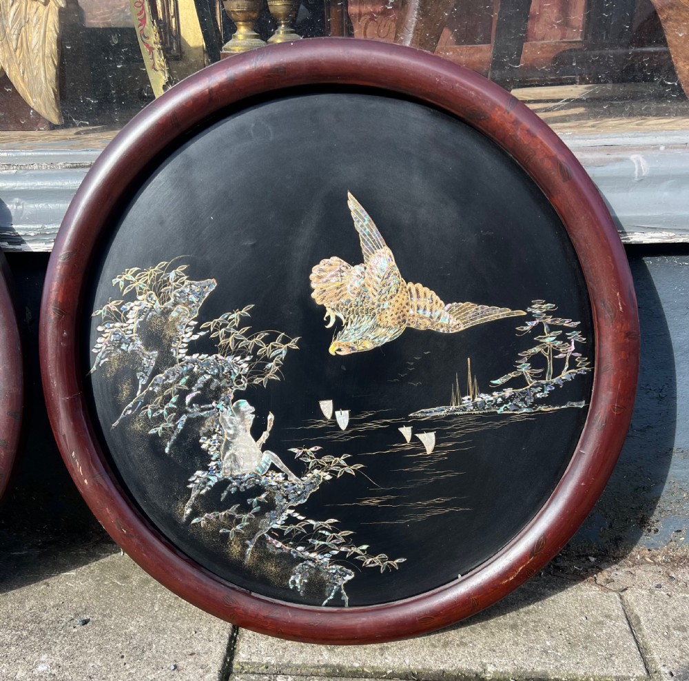 A pair of circular black lacquered wall plaques set in dark wood frames, decorated with mother-of-pearl and bone inlays depicting a peacock amongst foliage and a bird in flight over water. View II