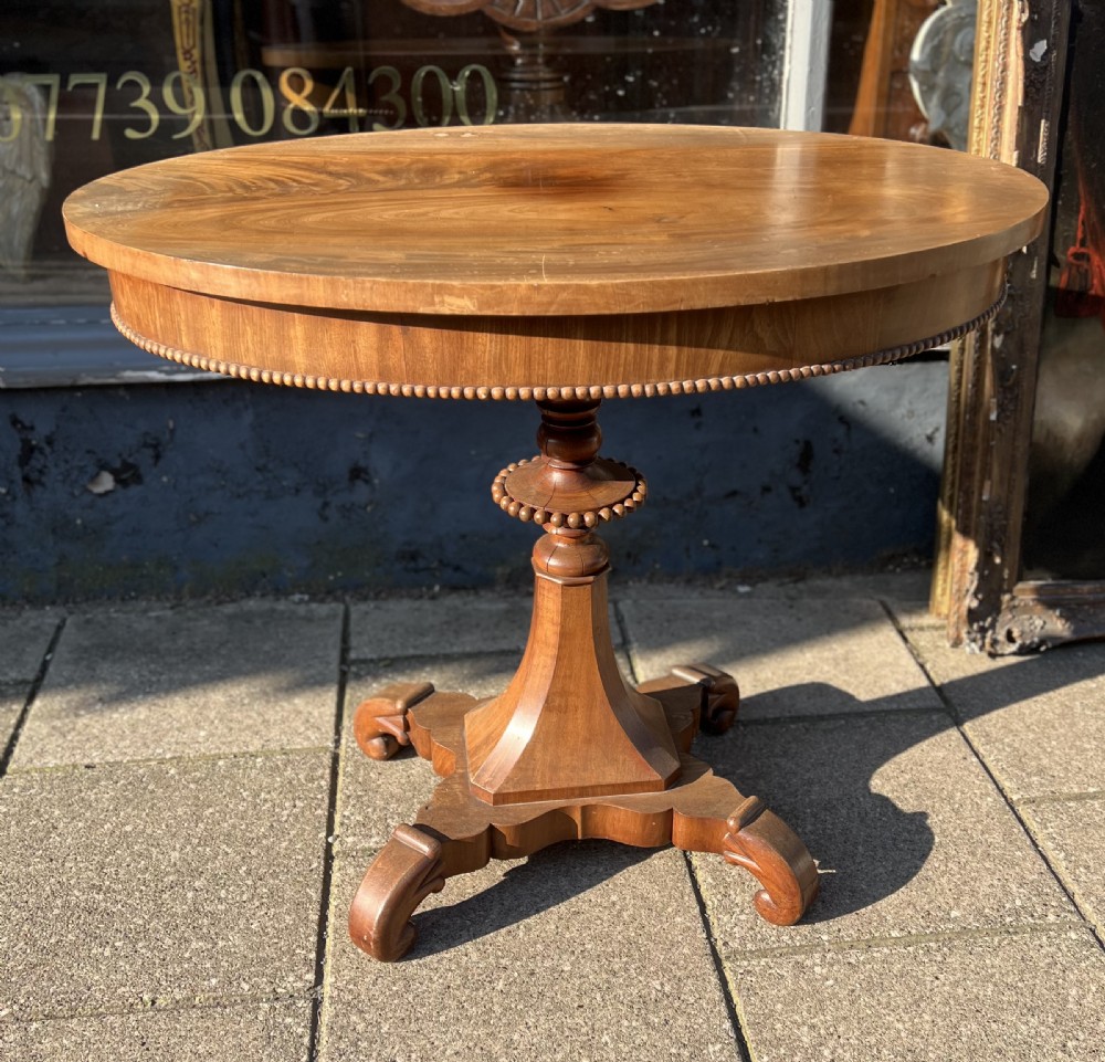 A nineteenth-century oval wooden occasional table featuring a beaded apron, turned central pedestal, and a four-legged scrolled base.