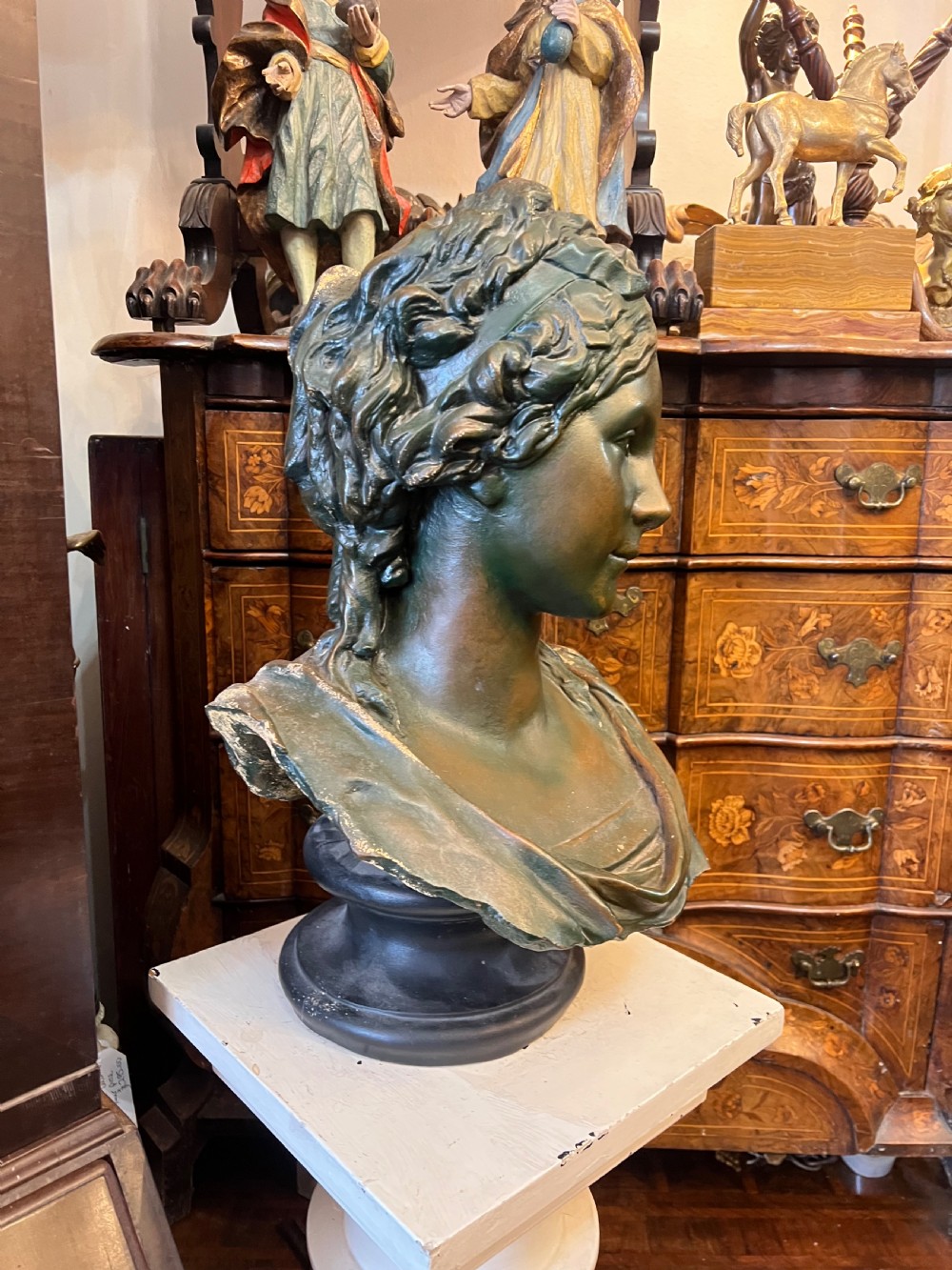 A bronzed terracotta bust of a classical woman featuring a green patinated surface, wavy pinned hair, draped garments, and a dark circular base. View II
