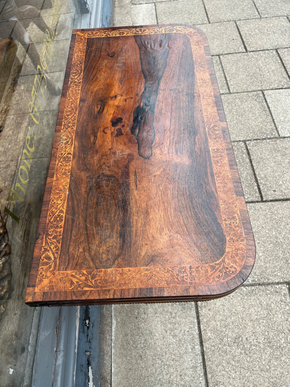 A Regency period rosewood fold-over tea table featuring intricate floral inlay along the border, resting on a pedestal base with four carved paw feet on castors. View III
