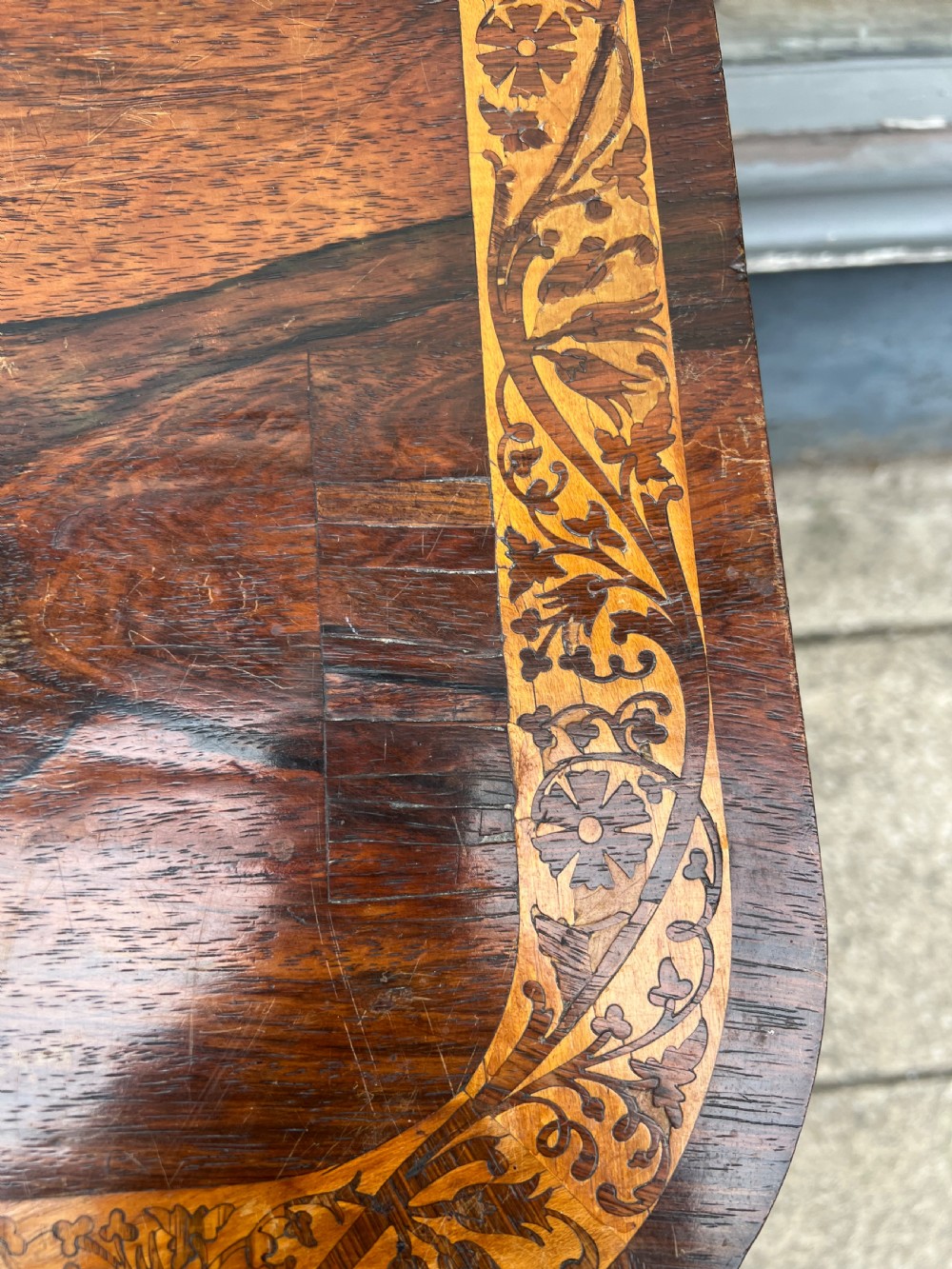 A Regency period rosewood fold-over tea table featuring intricate floral inlay along the border, resting on a pedestal base with four carved paw feet on castors. View V
