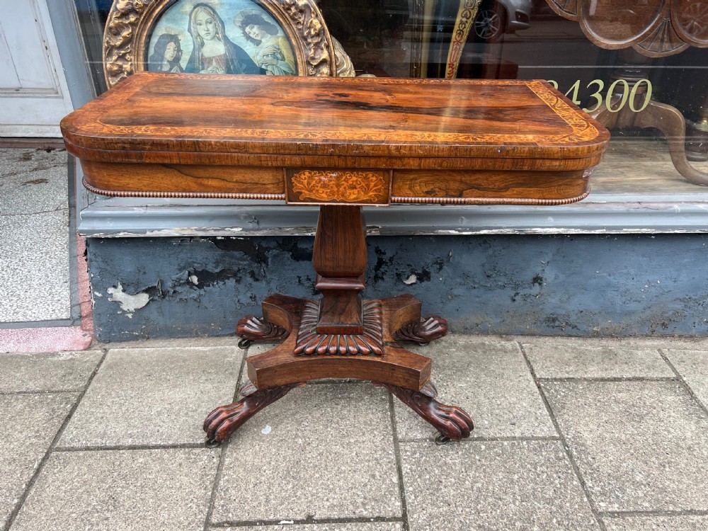 A Regency period rosewood fold-over tea table featuring intricate floral inlay along the border, resting on a pedestal base with four carved paw feet on castors. View VI