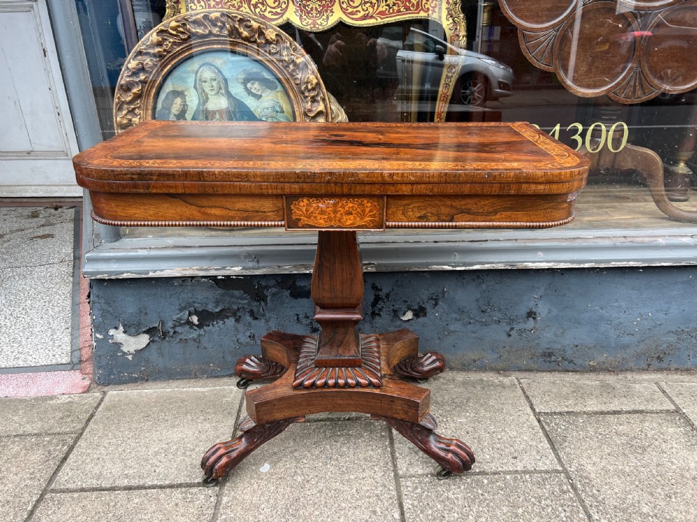 A Regency period rosewood fold-over tea table featuring intricate floral inlay along the border, resting on a pedestal base with four carved paw feet on castors. View VII