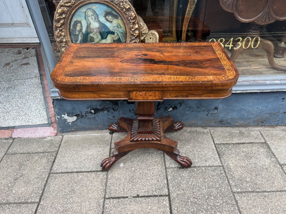 A Regency period rosewood fold-over tea table featuring intricate floral inlay along the border, resting on a pedestal base with four carved paw feet on castors. View VIII