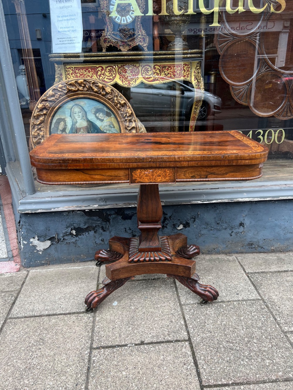 A Regency period rosewood fold-over tea table featuring intricate floral inlay along the border, resting on a pedestal base with four carved paw feet on castors. View IX