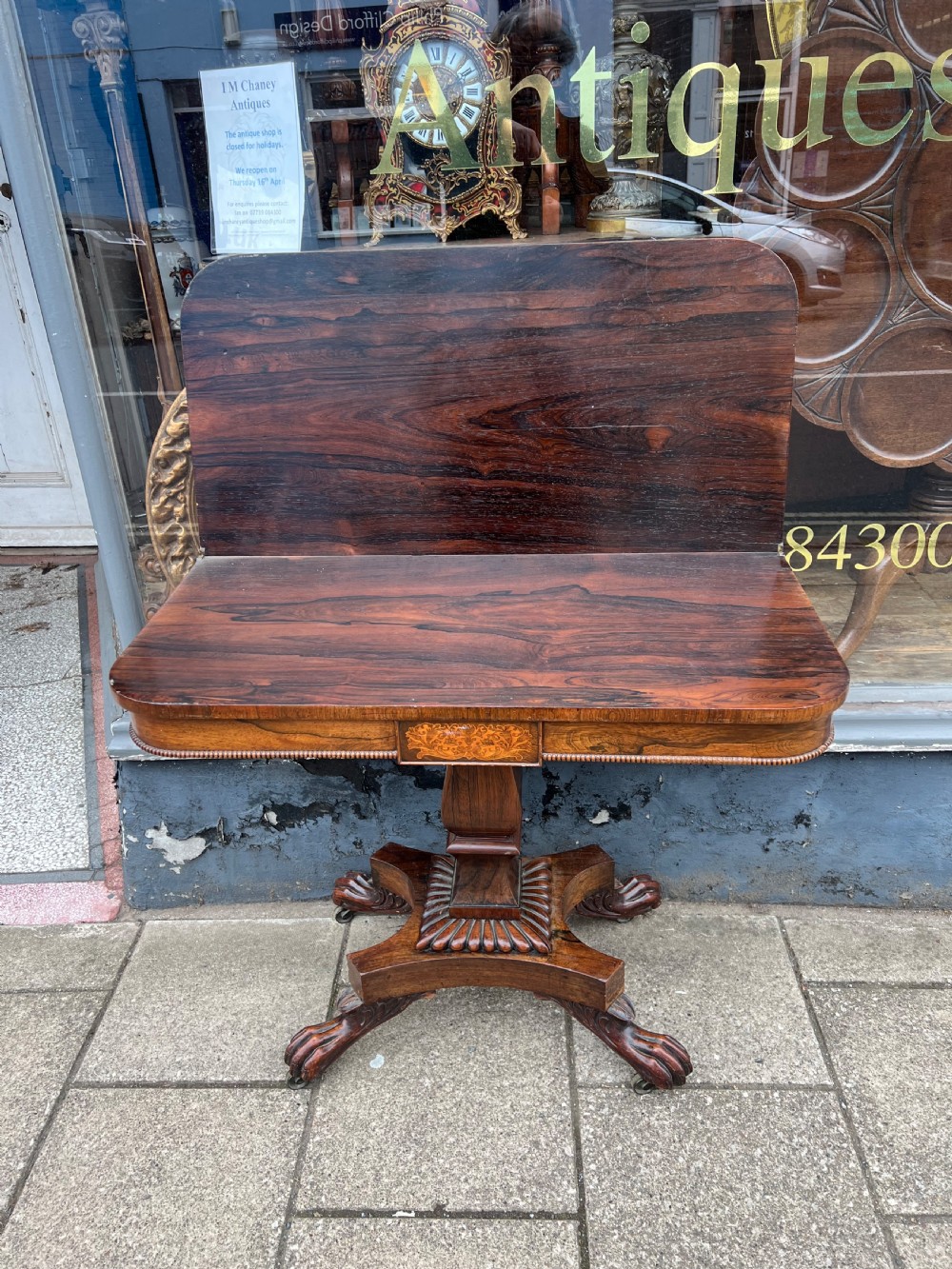 A Regency period rosewood fold-over tea table featuring intricate floral inlay along the border, resting on a pedestal base with four carved paw feet on castors. View X