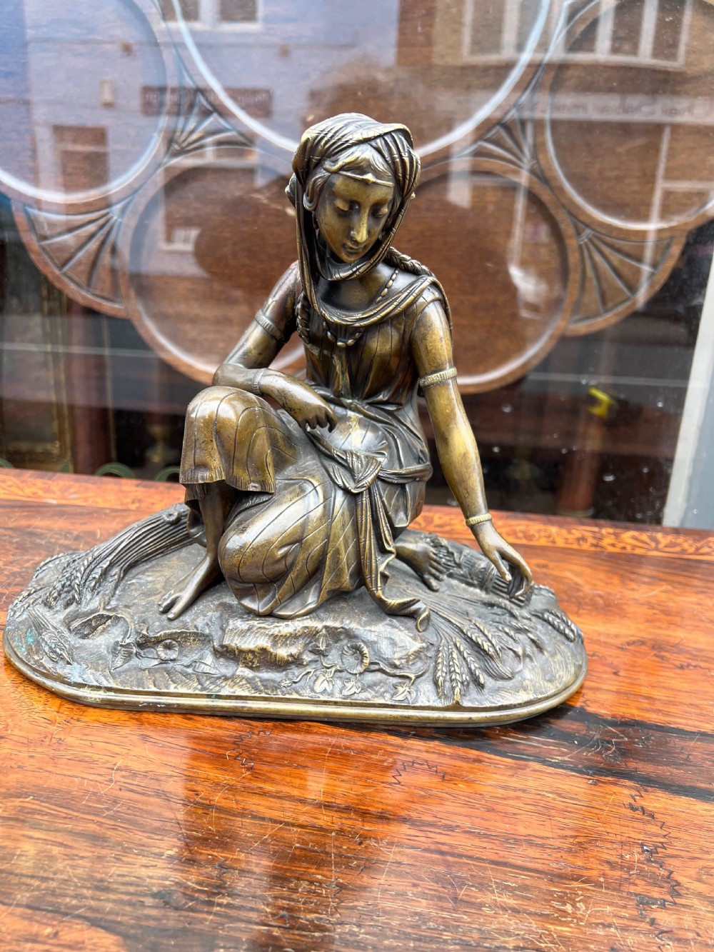 A 19th-century patinated bronze sculpture depicting a woman in draped traditional attire and headwrap crouching in a wheat field. View II
