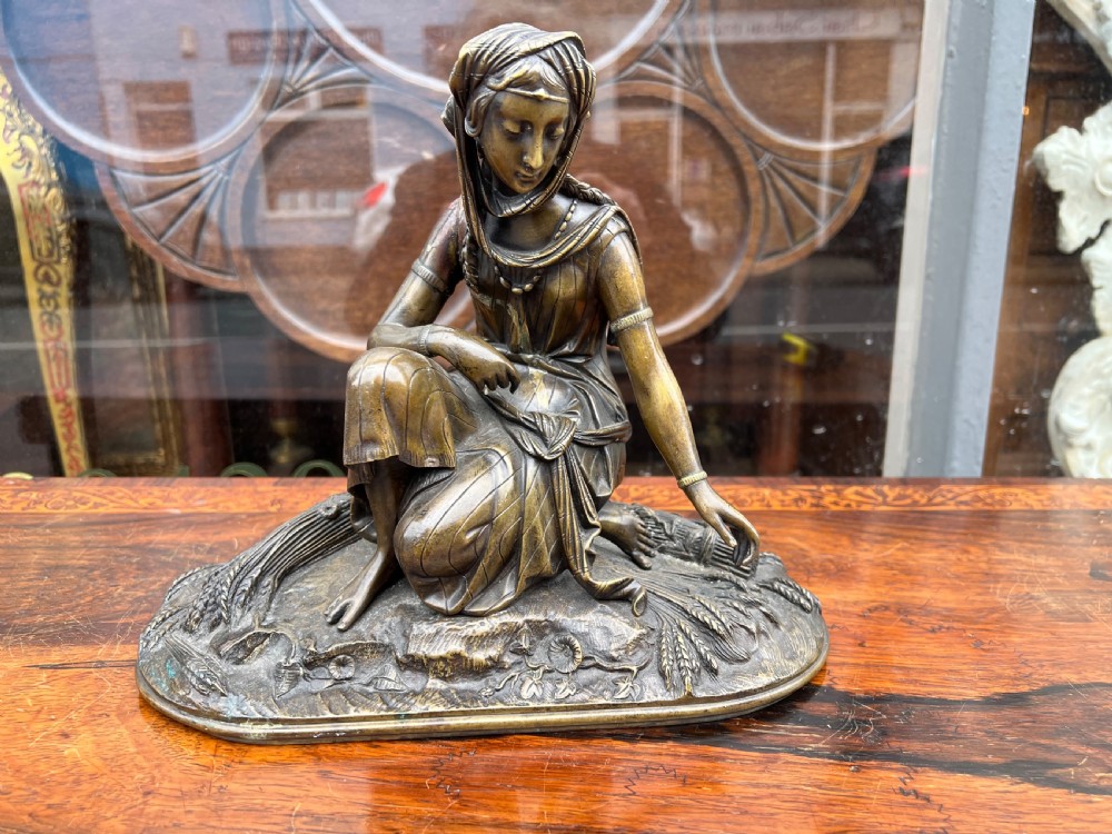 A 19th-century patinated bronze sculpture depicting a woman in draped traditional attire and headwrap crouching in a wheat field. View IV
