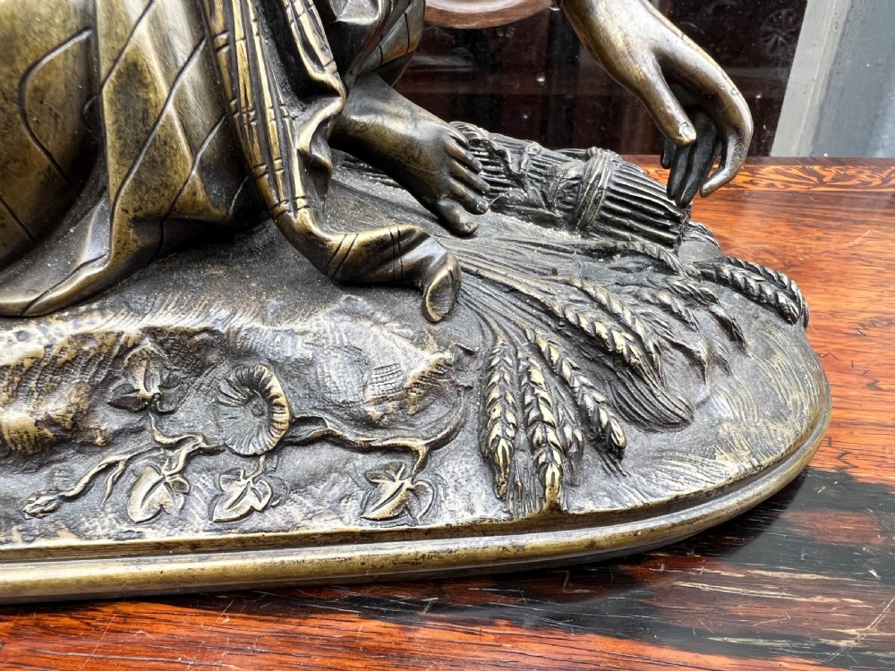 A 19th-century patinated bronze sculpture depicting a woman in draped traditional attire and headwrap crouching in a wheat field. View V