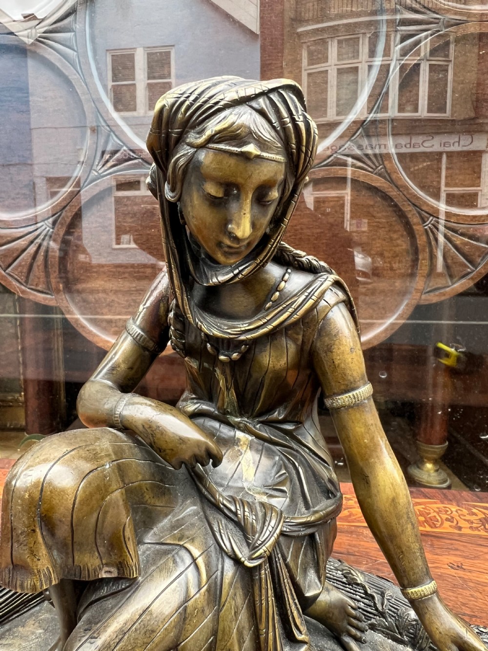 A 19th-century patinated bronze sculpture depicting a woman in draped traditional attire and headwrap crouching in a wheat field. View VI