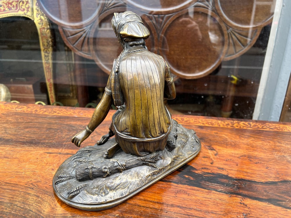 A 19th-century patinated bronze sculpture depicting a woman in draped traditional attire and headwrap crouching in a wheat field. View VII
