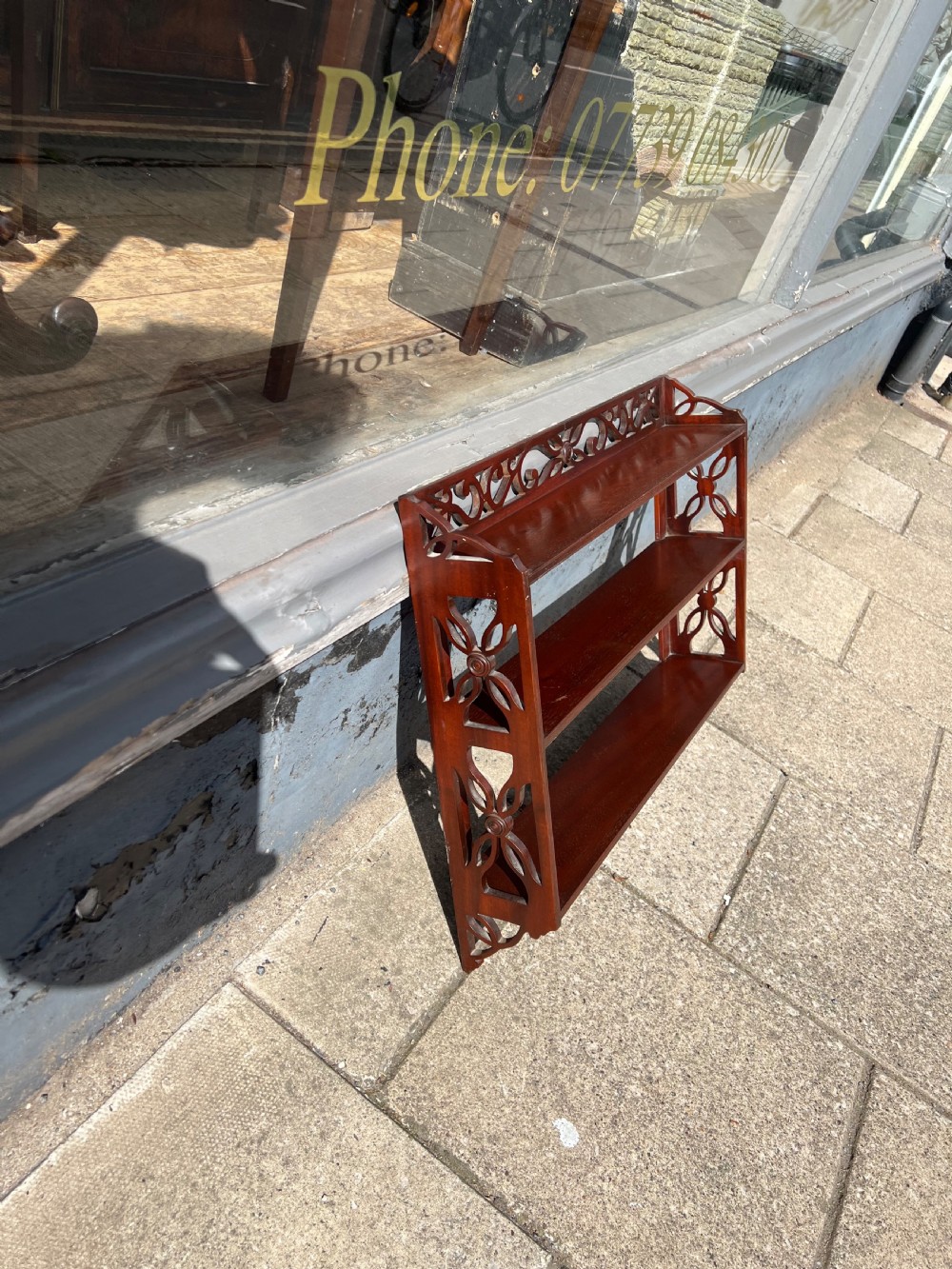 A three-tier dark mahogany wall shelf featuring decorative lattice fretwork side panels and a carved top gallery. View X