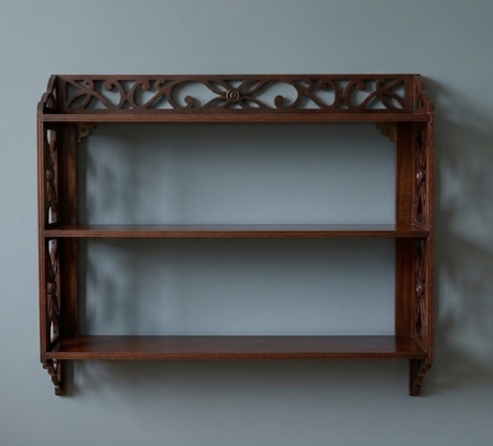 A three-tier dark mahogany wall shelf featuring decorative lattice fretwork side panels and a carved top gallery.