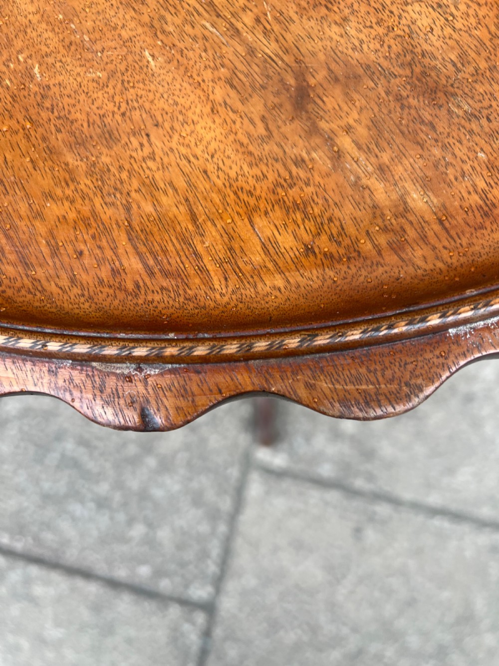 A nineteenth-century dark wood tripod wine table featuring a scalloped rim top, a turned central column, and three cabriole legs. View IV