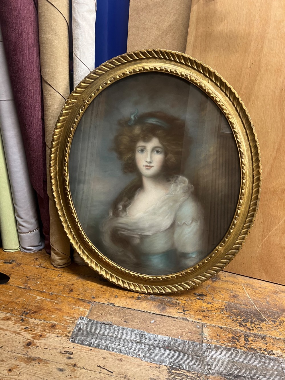 An oval giltwood framed pastel portrait of a young woman with voluminous hair, wearing a powder blue headband and soft cream drape. View III