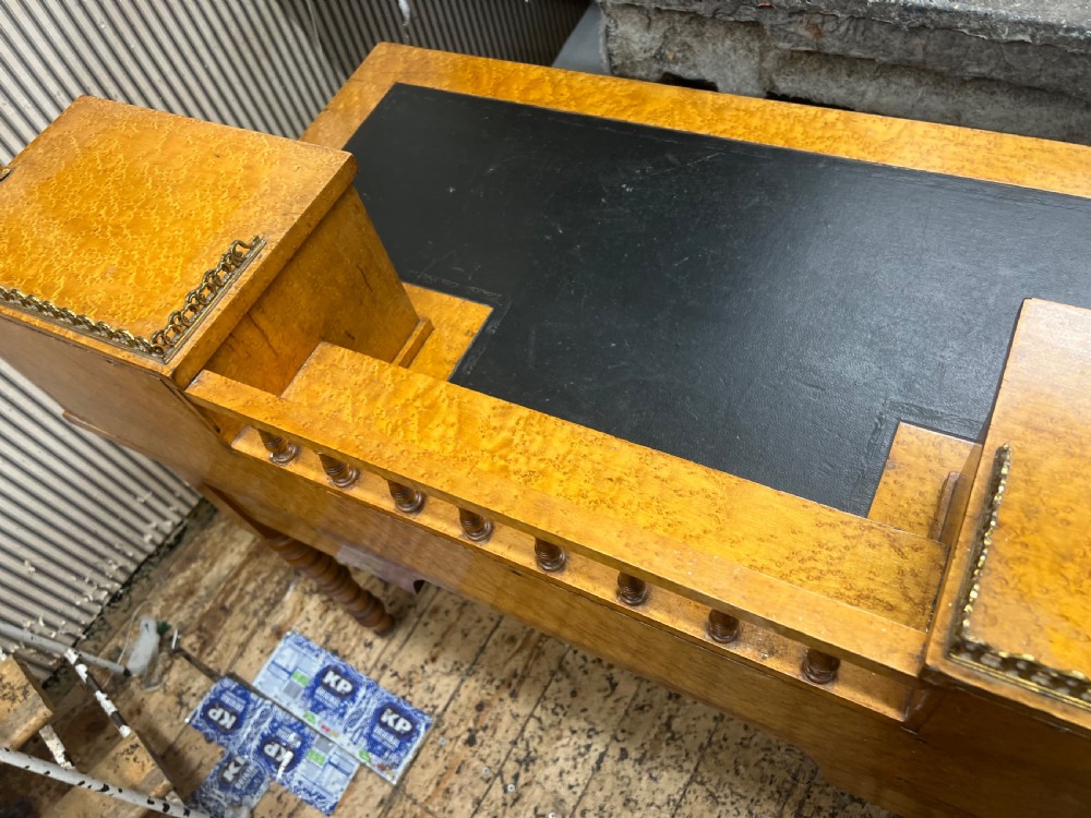 An antique birds eye maple writing desk featuring a black leather surface, turned legs on castors, and an upper superstructure with small drawers and a brass gallery railing. View III