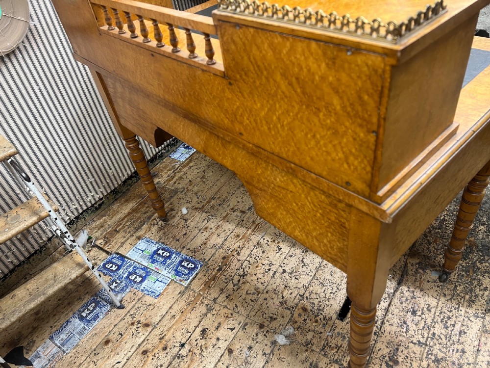 An antique birds eye maple writing desk featuring a black leather surface, turned legs on castors, and an upper superstructure with small drawers and a brass gallery railing. View V