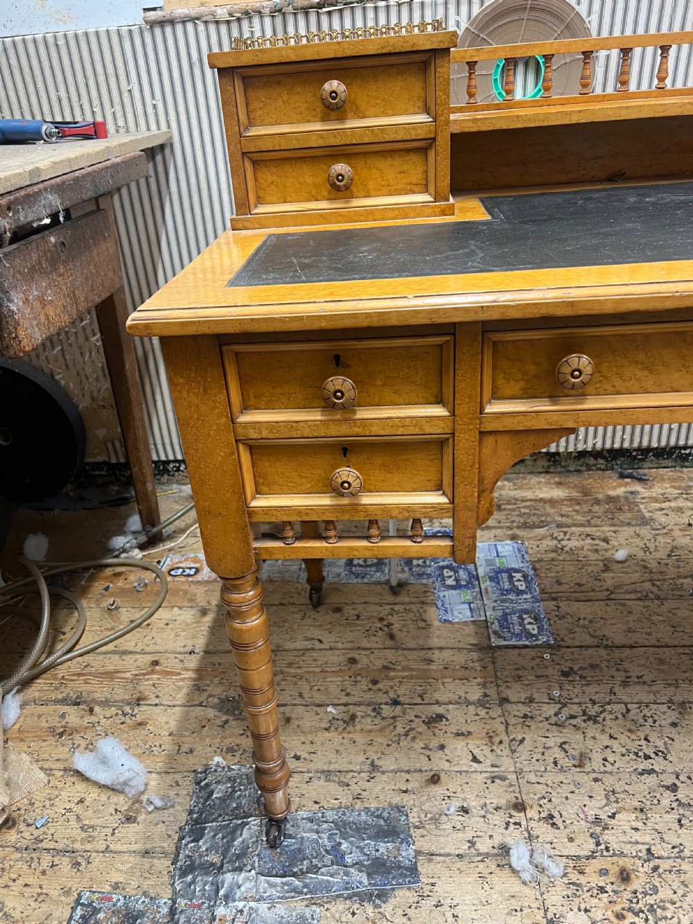 An antique birds eye maple writing desk featuring a black leather surface, turned legs on castors, and an upper superstructure with small drawers and a brass gallery railing. View VII