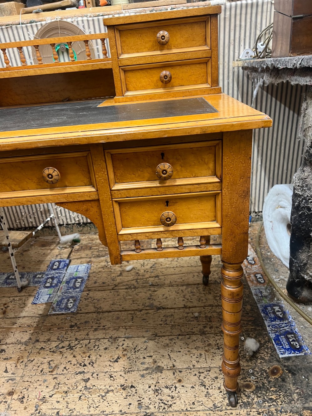 An antique birds eye maple writing desk featuring a black leather surface, turned legs on castors, and an upper superstructure with small drawers and a brass gallery railing. View IX