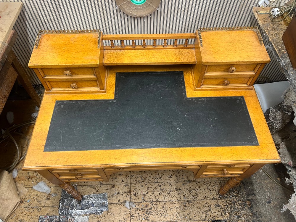 An antique birds eye maple writing desk featuring a black leather surface, turned legs on castors, and an upper superstructure with small drawers and a brass gallery railing. View X