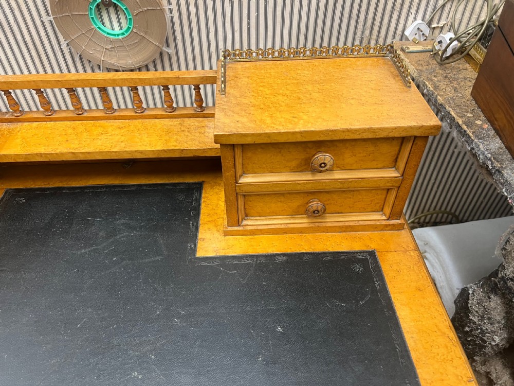 An antique birds eye maple writing desk featuring a black leather surface, turned legs on castors, and an upper superstructure with small drawers and a brass gallery railing. View XI