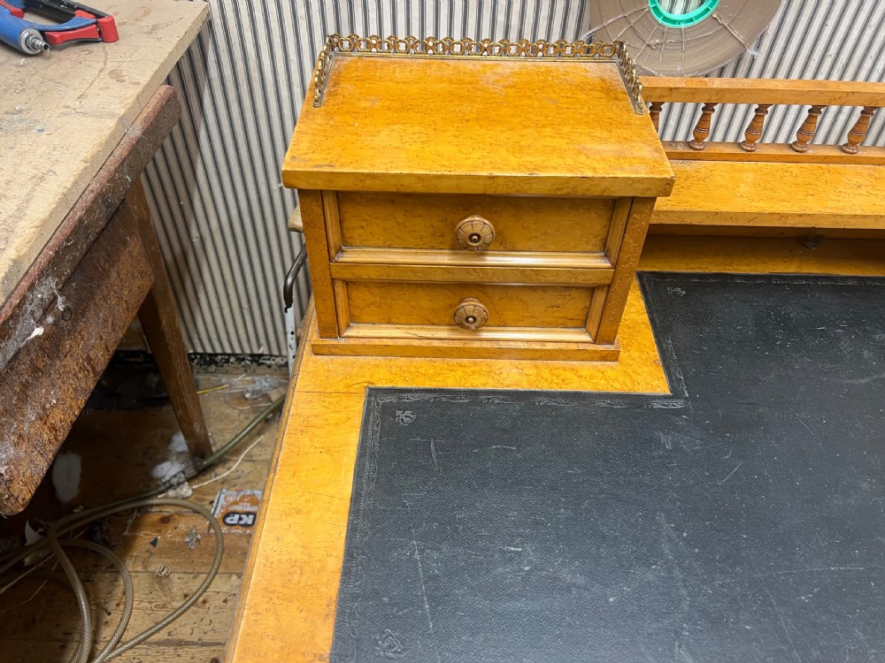 An antique birds eye maple writing desk featuring a black leather surface, turned legs on castors, and an upper superstructure with small drawers and a brass gallery railing. View XII