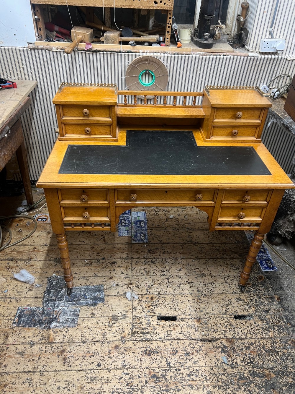 An antique birds eye maple writing desk featuring a black leather surface, turned legs on castors, and an upper superstructure with small drawers and a brass gallery railing. View XIII