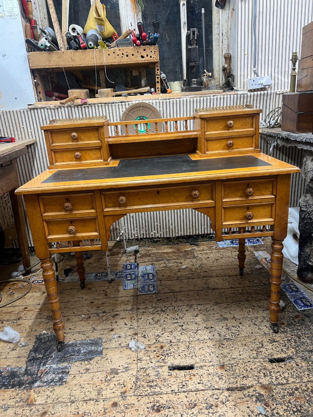 An antique birds eye maple writing desk featuring a black leather surface, turned legs on castors, and an upper superstructure with small drawers and a brass gallery railing. View XIV