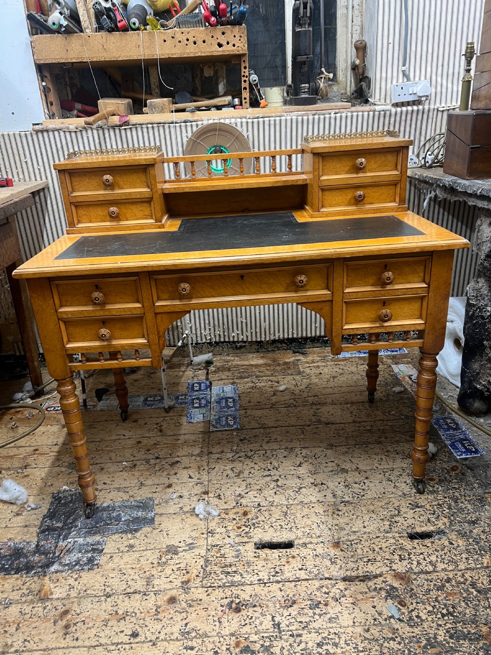 An antique birds eye maple writing desk featuring a black leather surface, turned legs on castors, and an upper superstructure with small drawers and a brass gallery railing. View XV