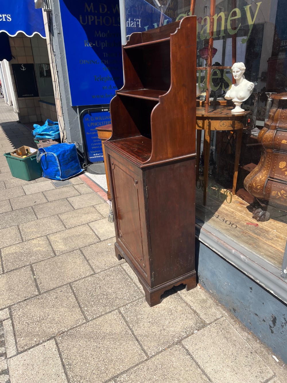 A dark mahogany Georgian waterfall bookcase featuring graduated open shelves above a single panelled cupboard door resting on bracket feet. View IV