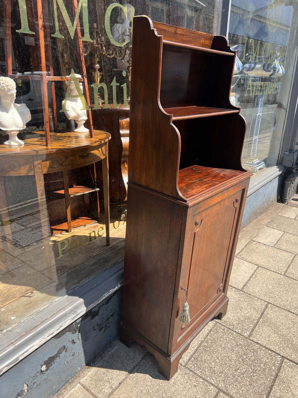 A dark mahogany Georgian waterfall bookcase featuring graduated open shelves above a single panelled cupboard door resting on bracket feet. View V