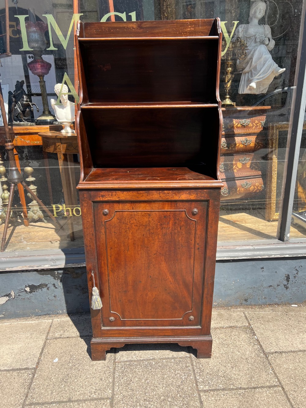 A dark mahogany Georgian waterfall bookcase featuring graduated open shelves above a single panelled cupboard door resting on bracket feet. View VI