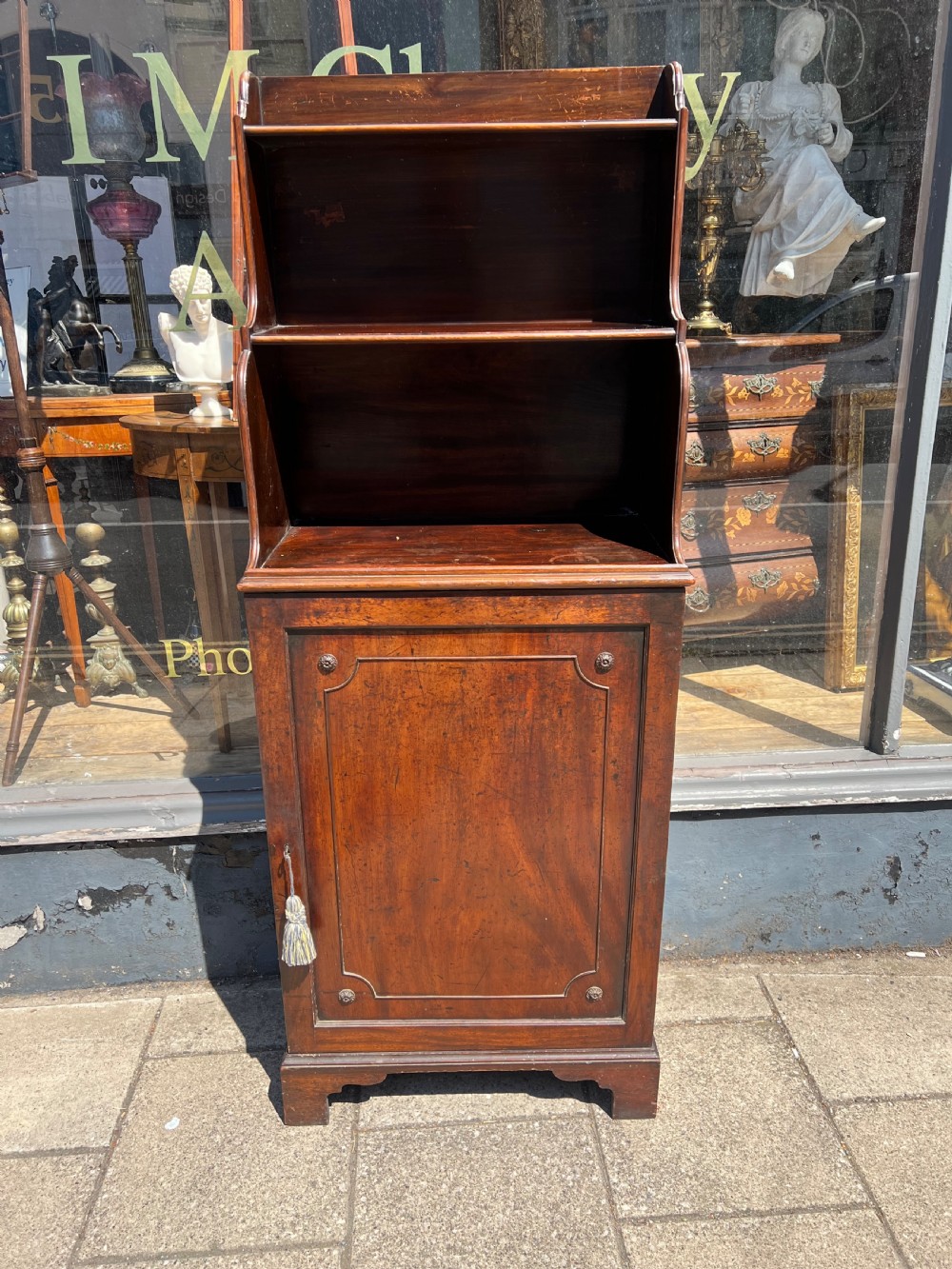A dark mahogany Georgian waterfall bookcase featuring graduated open shelves above a single panelled cupboard door resting on bracket feet. View VII