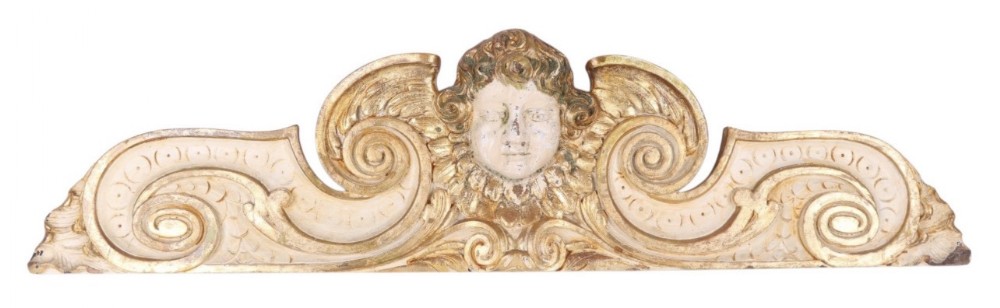 A wide carved wooden architectural overdoor featuring a central cherub face flanked by scrolling volutes in cream and gold finish.