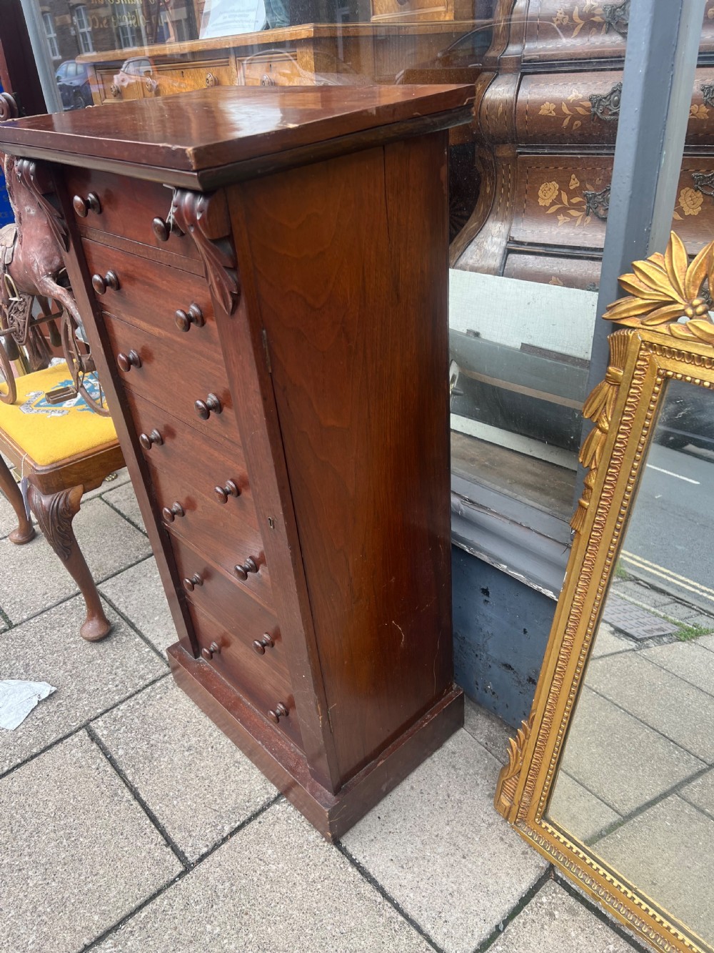 A tall, narrow Victorian walnut Wellington chest featuring seven stacked drawers with wooden turned knobs and carved leaf corbels at the top sides. View IV