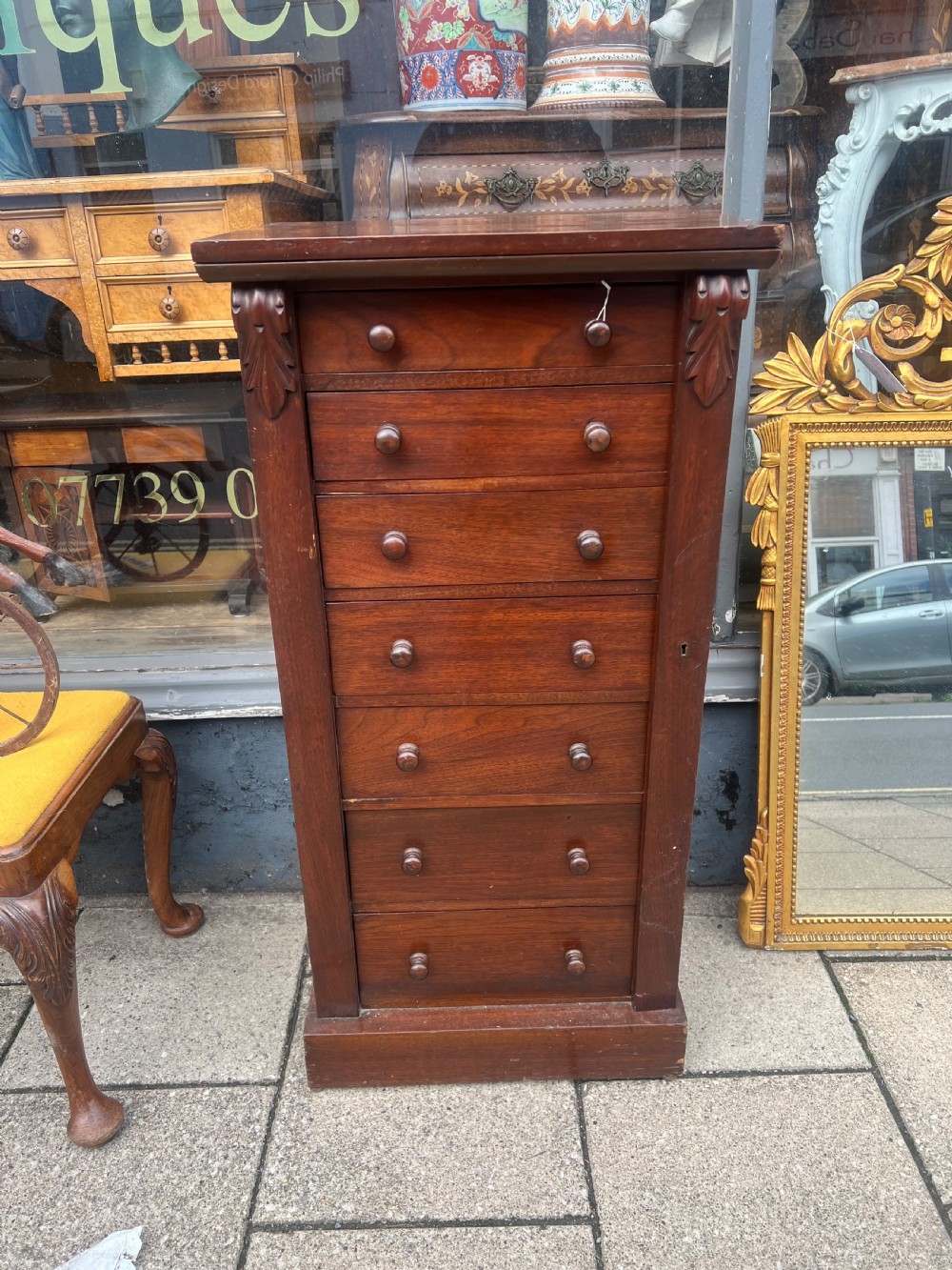A tall, narrow Victorian walnut Wellington chest featuring seven stacked drawers with wooden turned knobs and carved leaf corbels at the top sides. View V