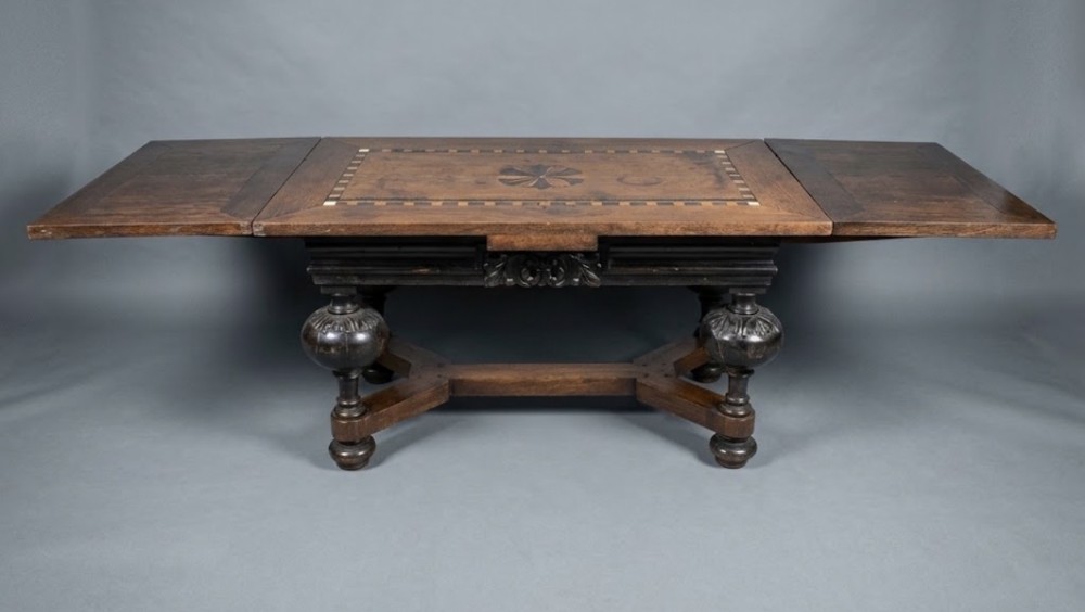 A 17th-century Dutch dark oak draw-leaf dining table with geometric inlay on top, carved bulbous legs, and an X-shaped stretcher.