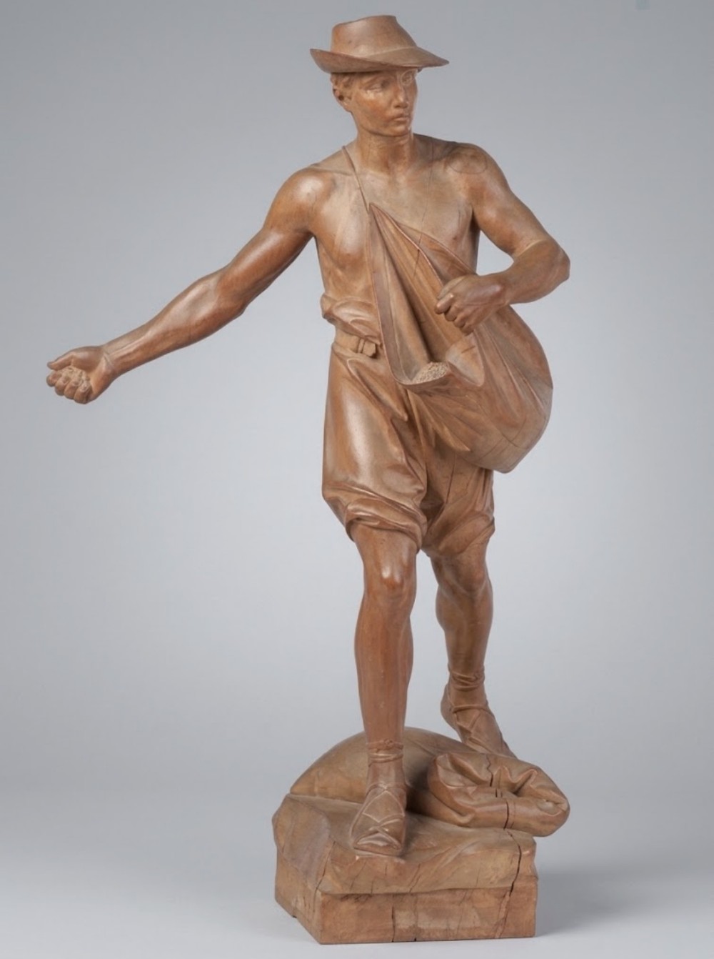 A carved fruitwood figure depicting a male sower striding forward with a seed bag over his shoulder on a carved base.