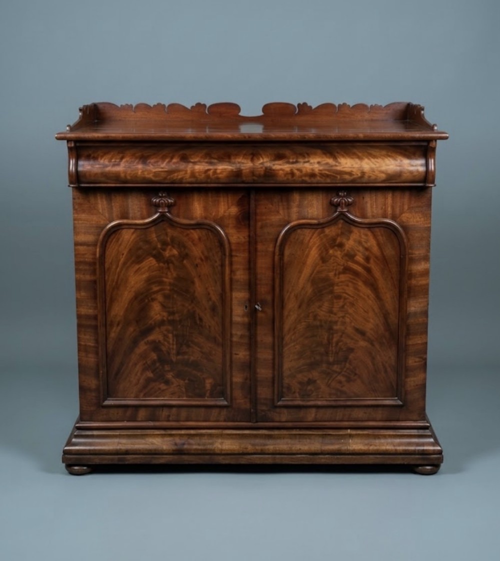 A William IV flame mahogany side cabinet with twin arch-panelled doors, a cushion frieze drawer, and a shaped gallery top rail.