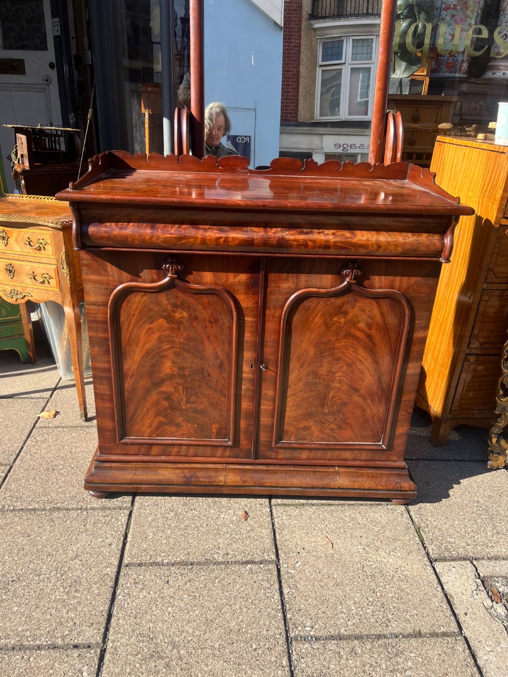 A William IV flame mahogany side cabinet with twin arch-panelled doors, a cushion frieze drawer, and a shaped gallery top rail. View II