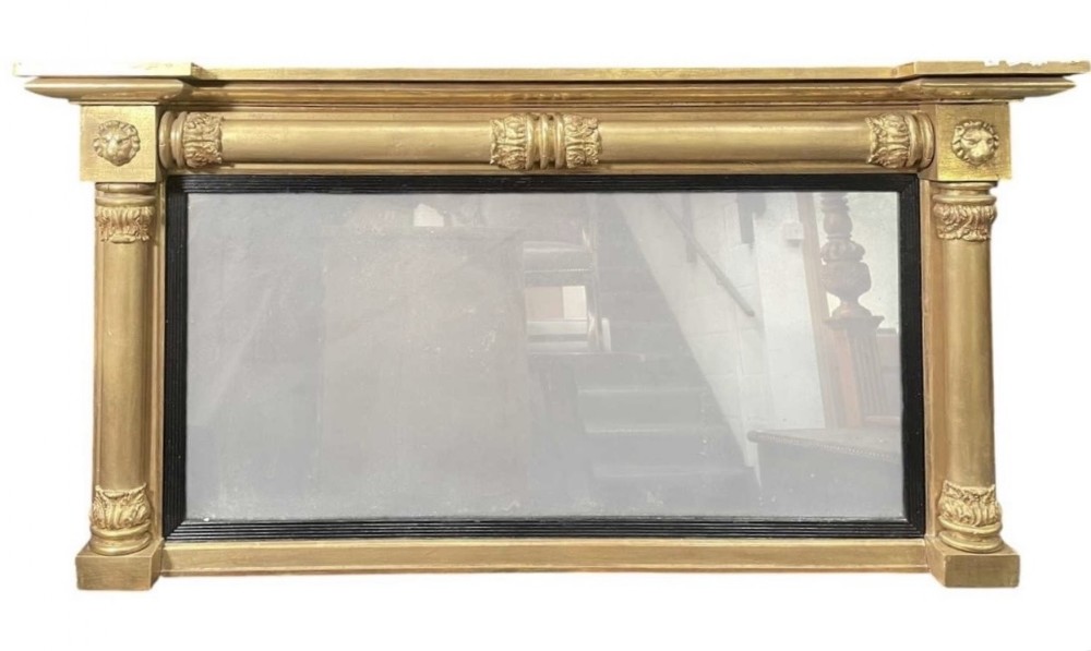 A horizontal Regency giltwood overmantel mirror featuring side pilasters, carved lion mask details, and an ebonised inner slip.