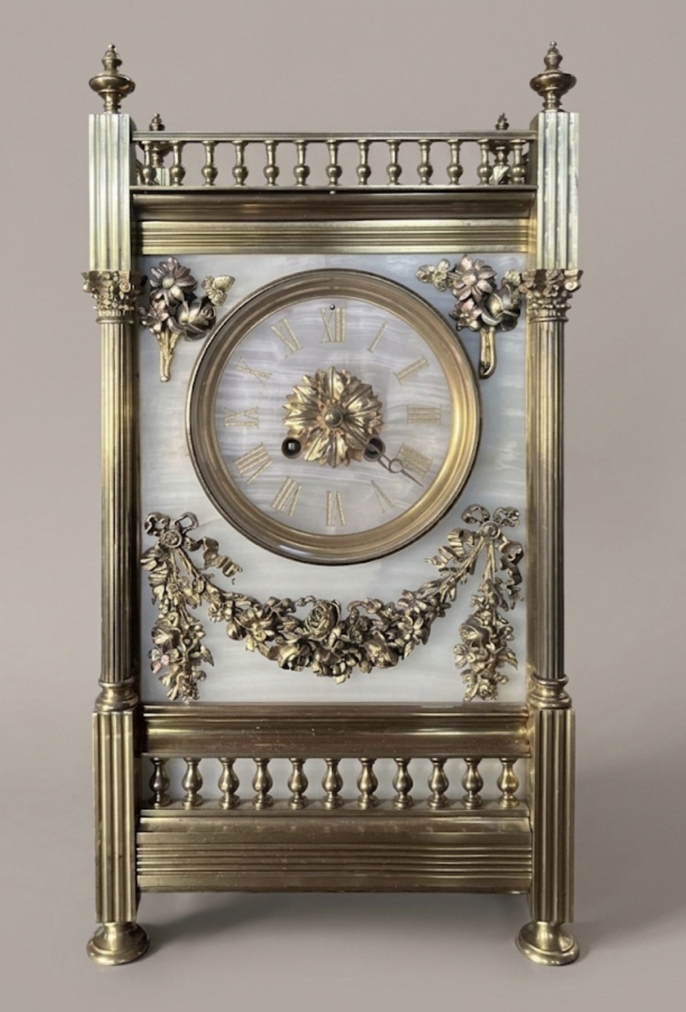 A nineteenth-century French gilt brass and white alabaster mantel clock featuring fluted corner columns, a balustrade top gallery, and floral swags surrounding the circular dial.
