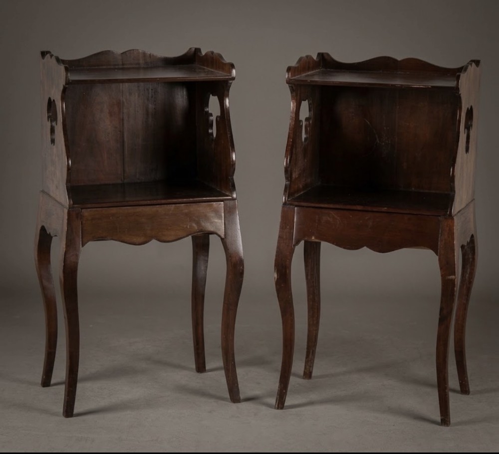 A pair of dark wood French Provincial bedside tables featuring slender cabriole legs, open shelf compartments, and scalloped top galleries with decorative cut-out handles.