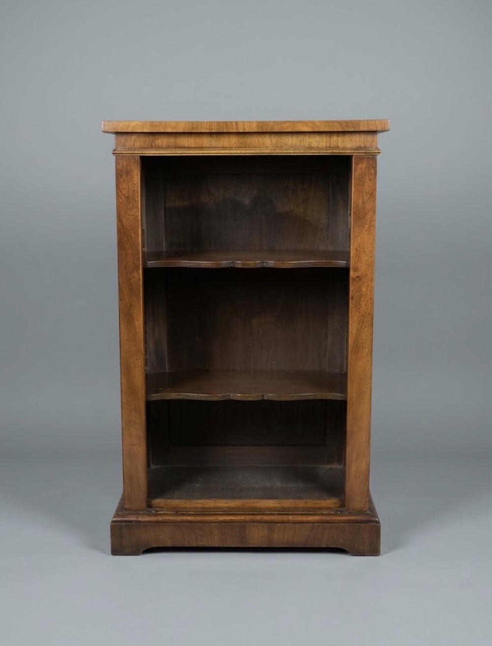 A small nineteenth-century mahogany open bookcase featuring three tiers with shaped shelf fronts and a plinth base.