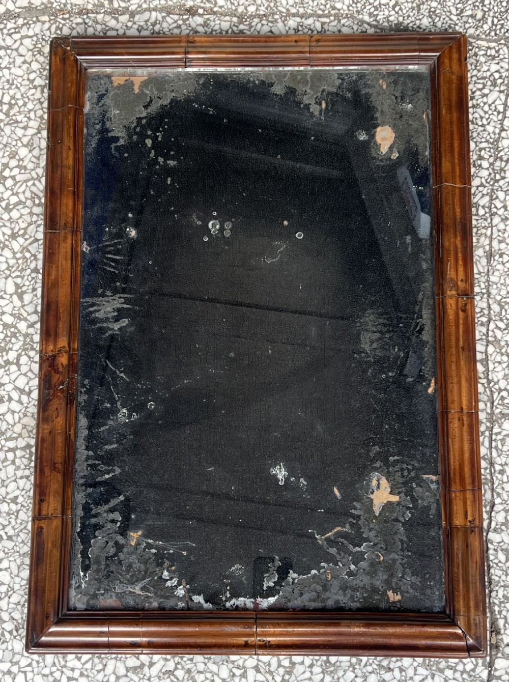 A rectangular 18th-century wall mirror featuring a moulded warm brown walnut wood frame enclosing heavily foxed and distressed glass.
